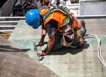 Carpenter with blue hard hat fixing roof with hammer and nails.
