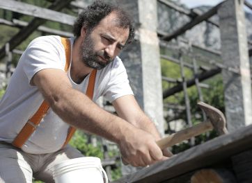 A carpenter using a hammer to drive nails into wood at an outdoor construction site.