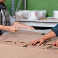 Workers packing sofa furniture in a box.